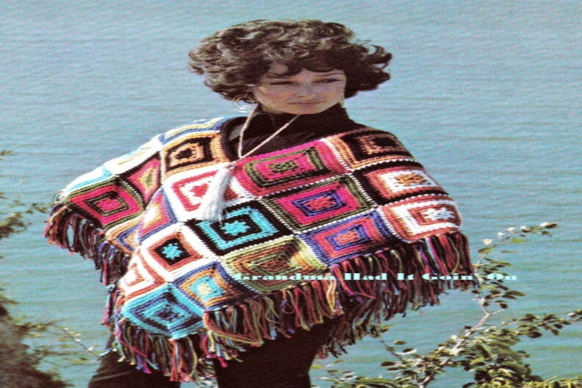 Brunette woman wearing a colorful poncho made up of granny squares and tassels along the bottom with a small v-neck.