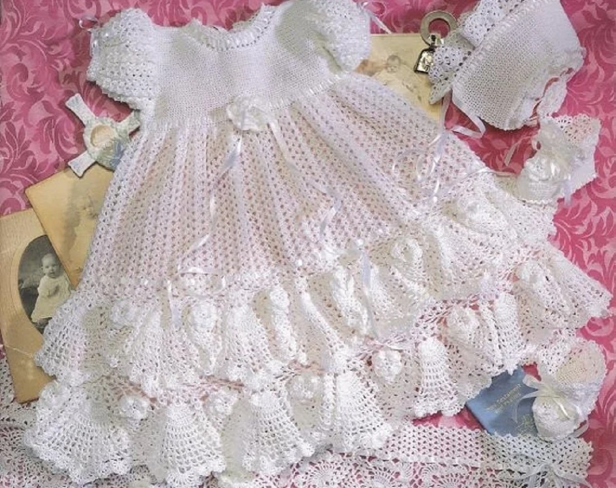 White crochet christening style dress with a bow around the waist and two ruffles along the bottom of the dress.