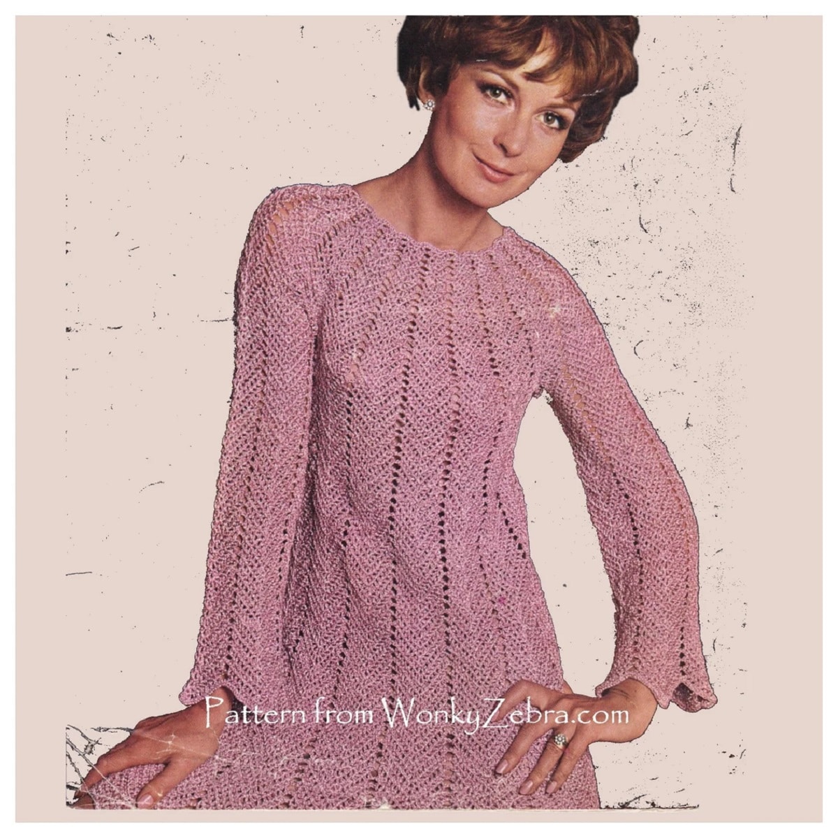 Brunette woman wearing a pink long sleeved crochet mini dress with vertical zig zags on a cream background.