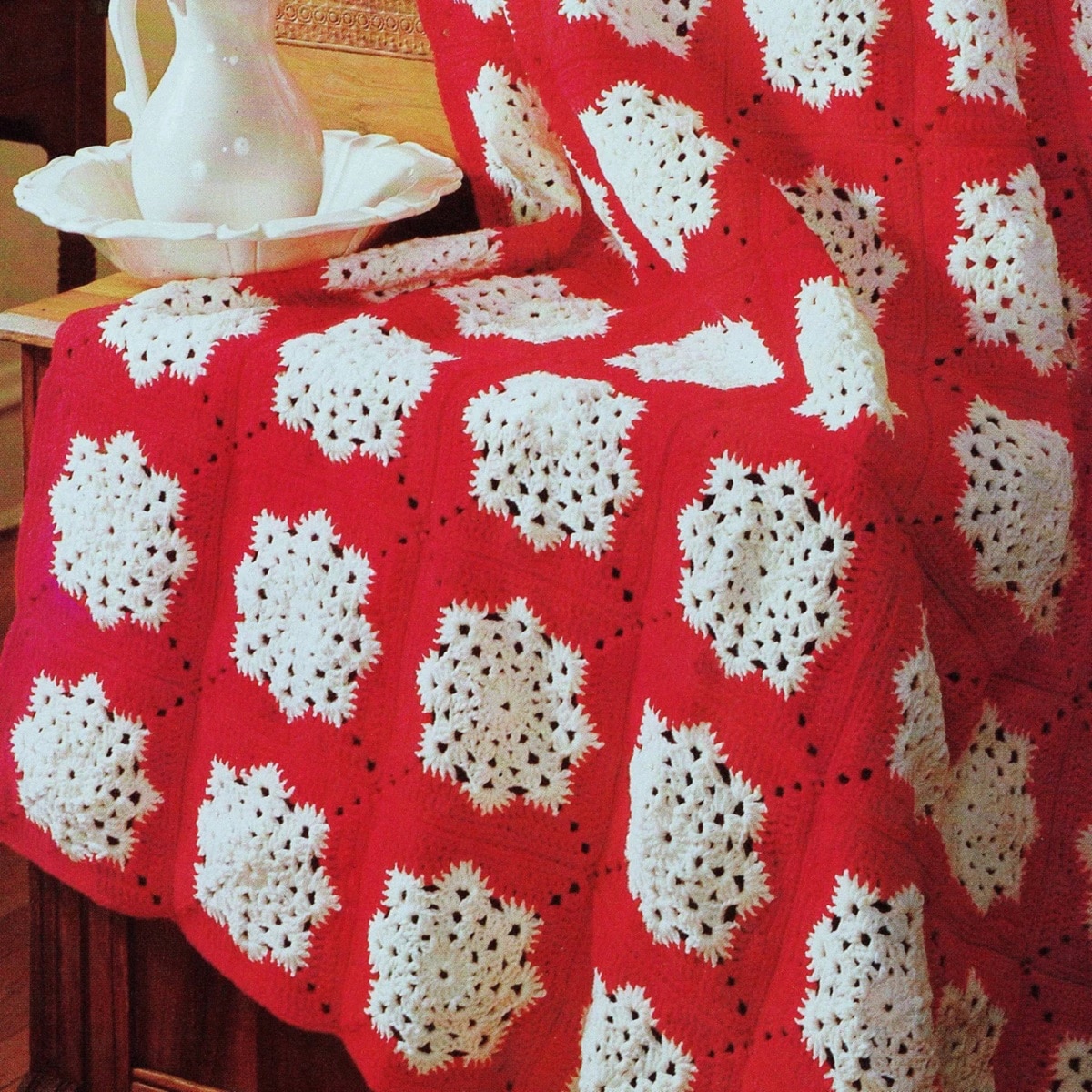 A red crochet blanket with white snowflakes in horizontal lines across the entire blanket draped over a chair.