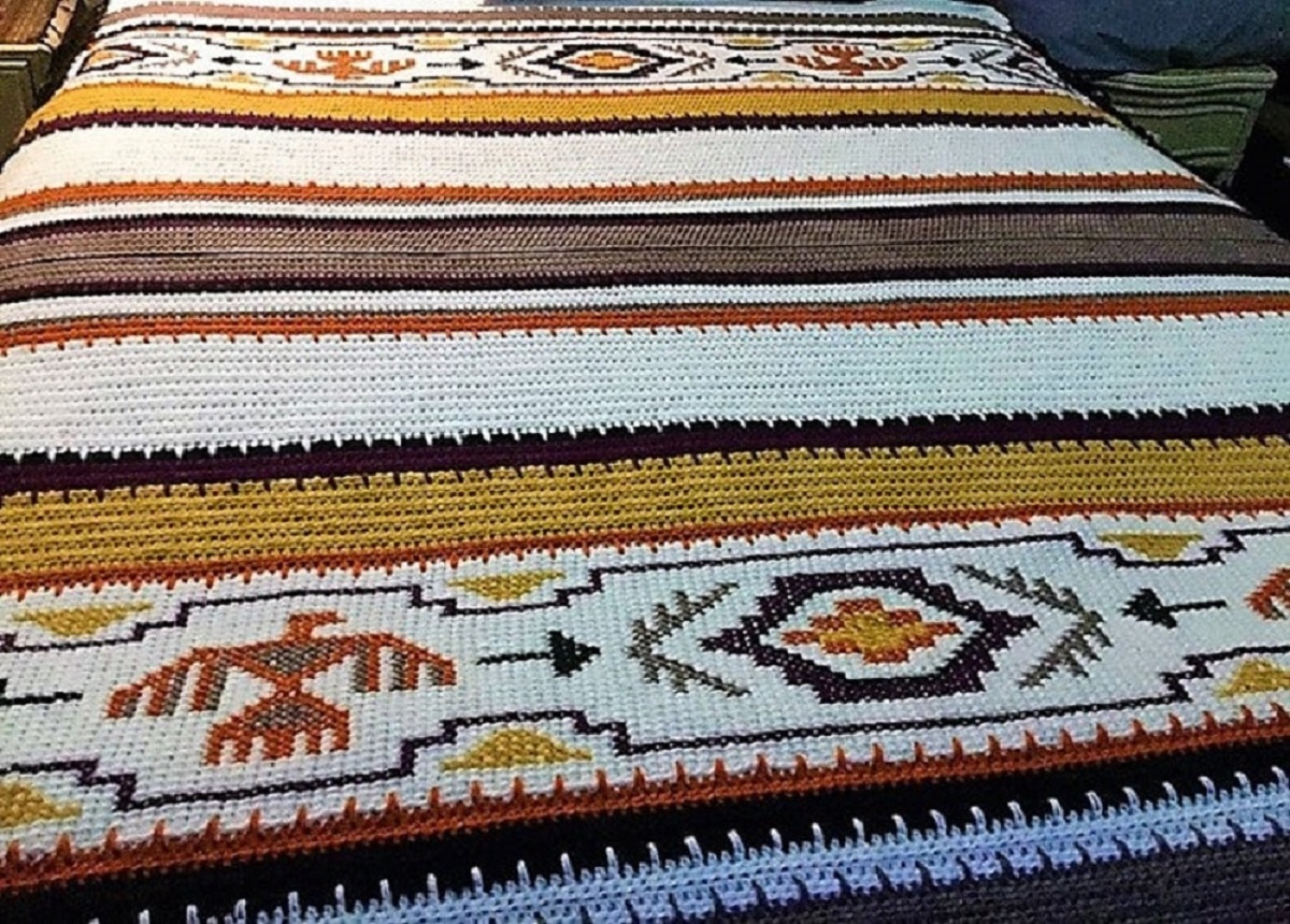 White, yellow, brown, and black striped crochet blanket with Native American designs on the bottom spread across a bed