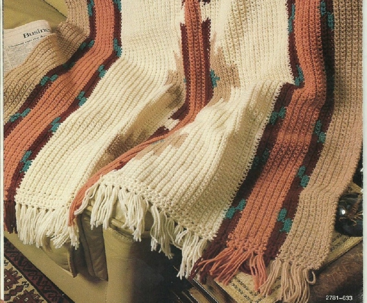 Brown, orange, black, and cream striped blanket with short tassels along the bottom folded on a chair. 