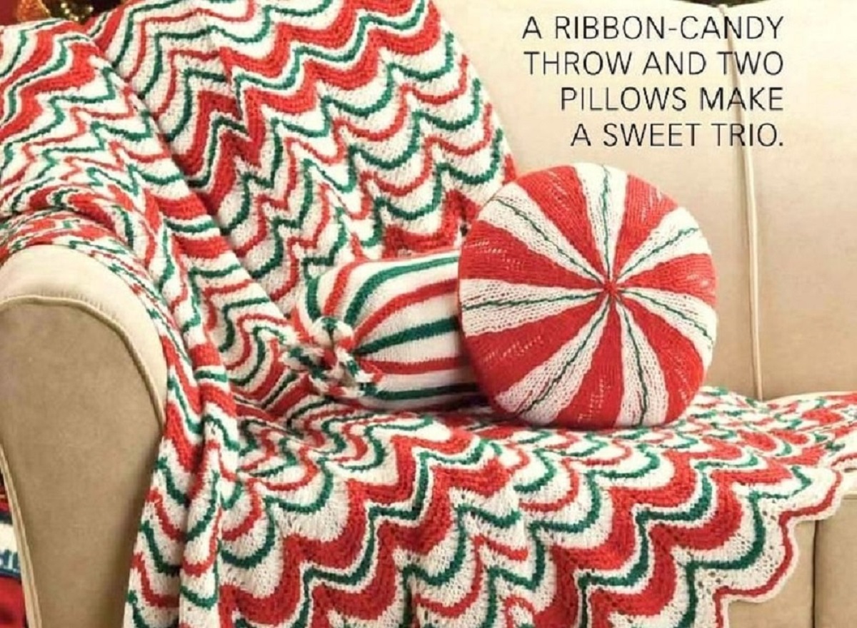 Red, white, and green wave style stripes across the whole crochet Afghan with red and white and red, white and green cushions on top. 