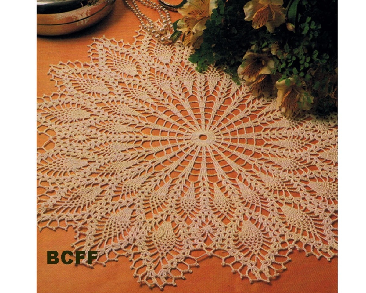 Large round cream doily with a round center and pineapples shooting off on long stems laid on a coral background.
