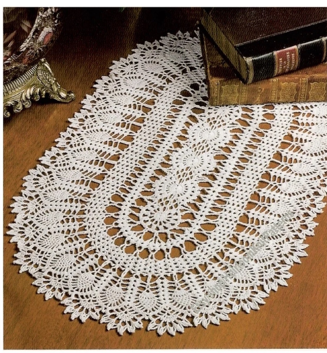 White pineapple doily featuring a slight trim on a wooden table with some leather bound books in the top corner.