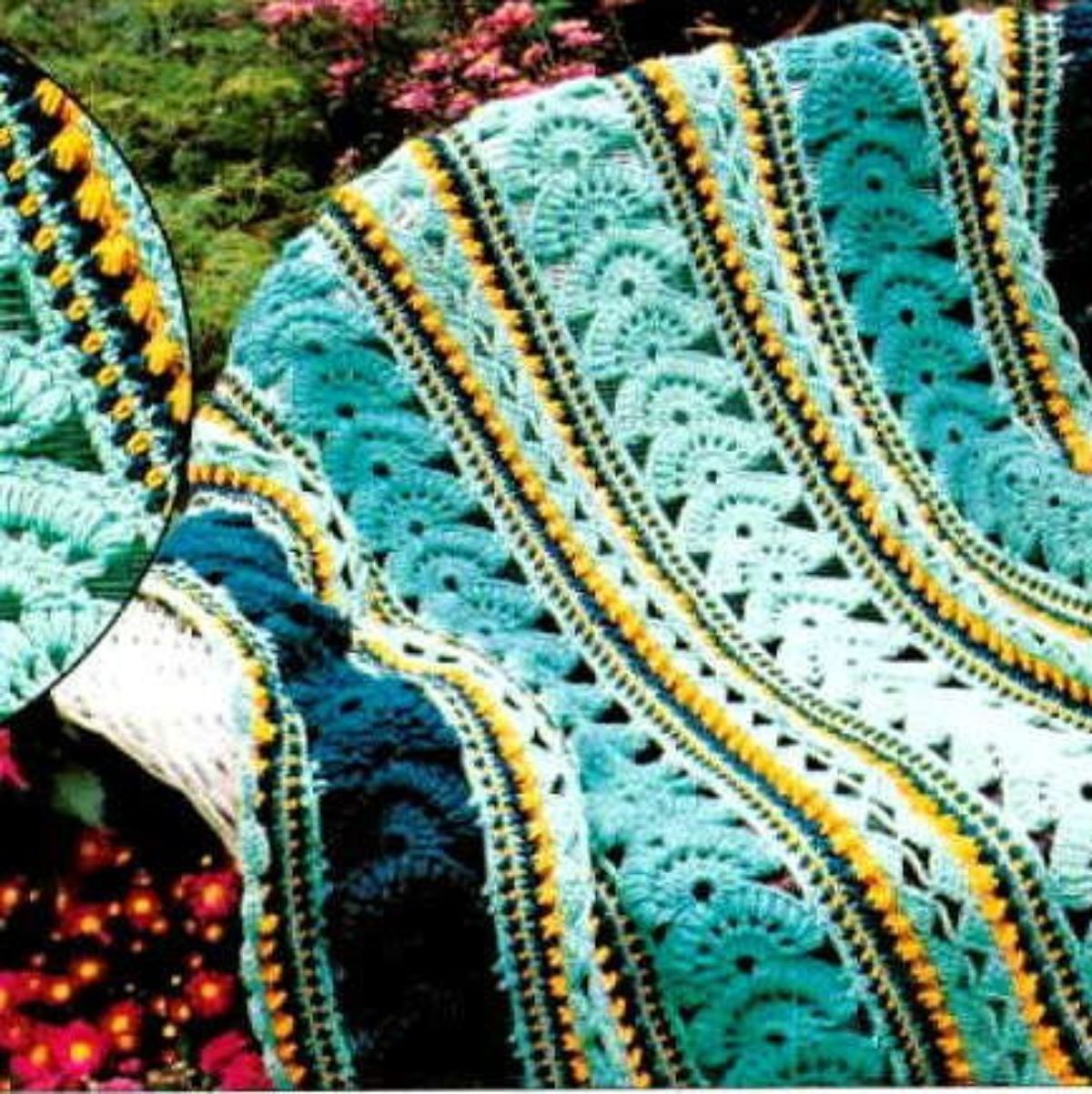 1920s style blue, yellow, and black striped crochet blanket with fan style stitching draped over a chair with grass and flowers behind. 