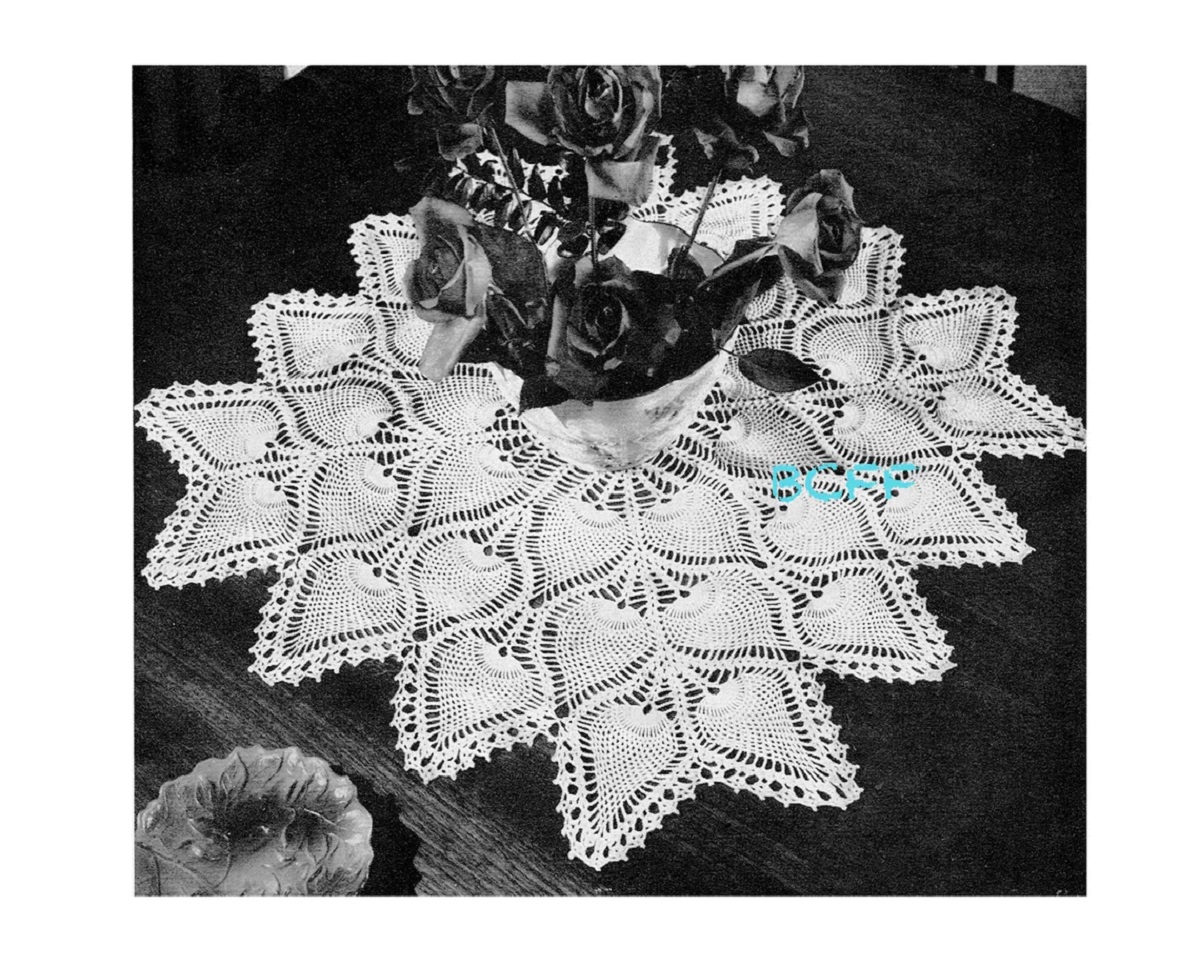 Large white square doily packed with petals filled with pineapples and small circles around the petals on the edge with a vase of flowers on top.