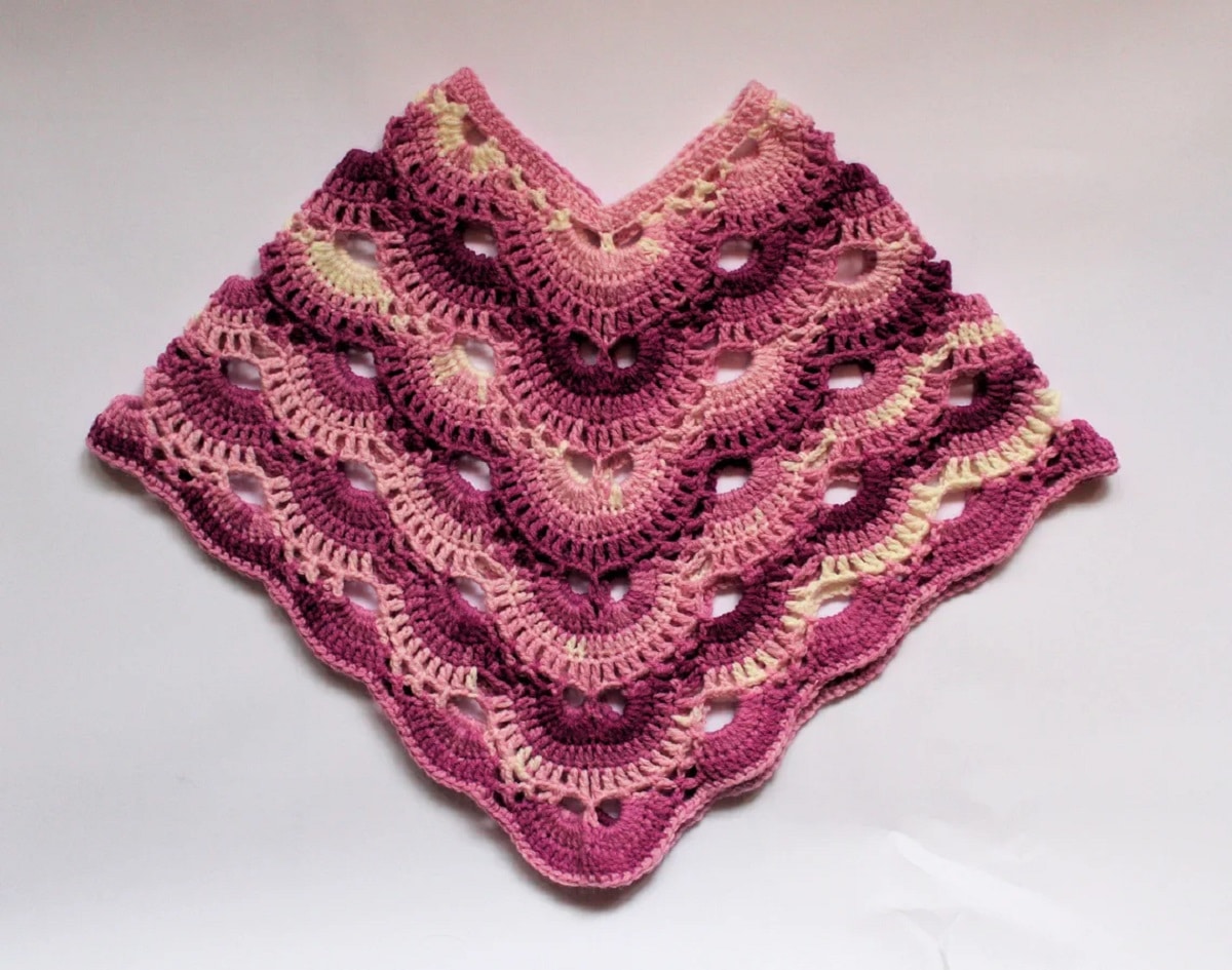 with two light purple tassels on either side. A pink, purple, and cream virus pattern poncho with thick diagonal stripes for each color on a white background.
