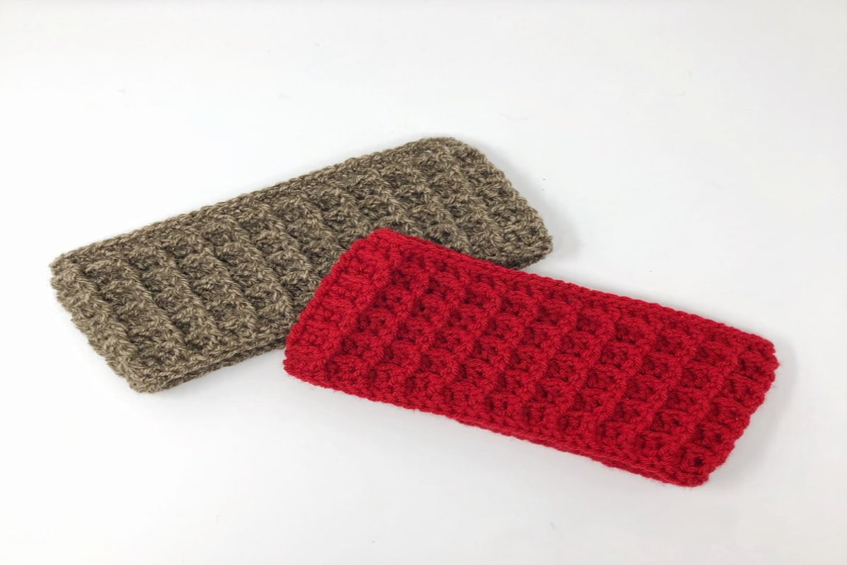 Red waffle stitch crochet headband next to a sage green waffle stitch headband on a white background.