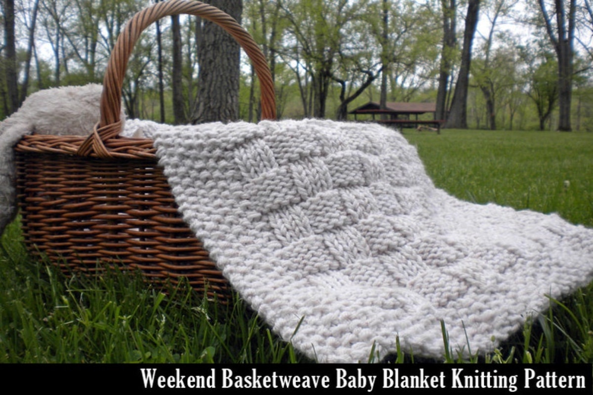 White basketweave crochet blanket with a thick white trim with small bobbles on, falling out of a wicker picnic basket.
