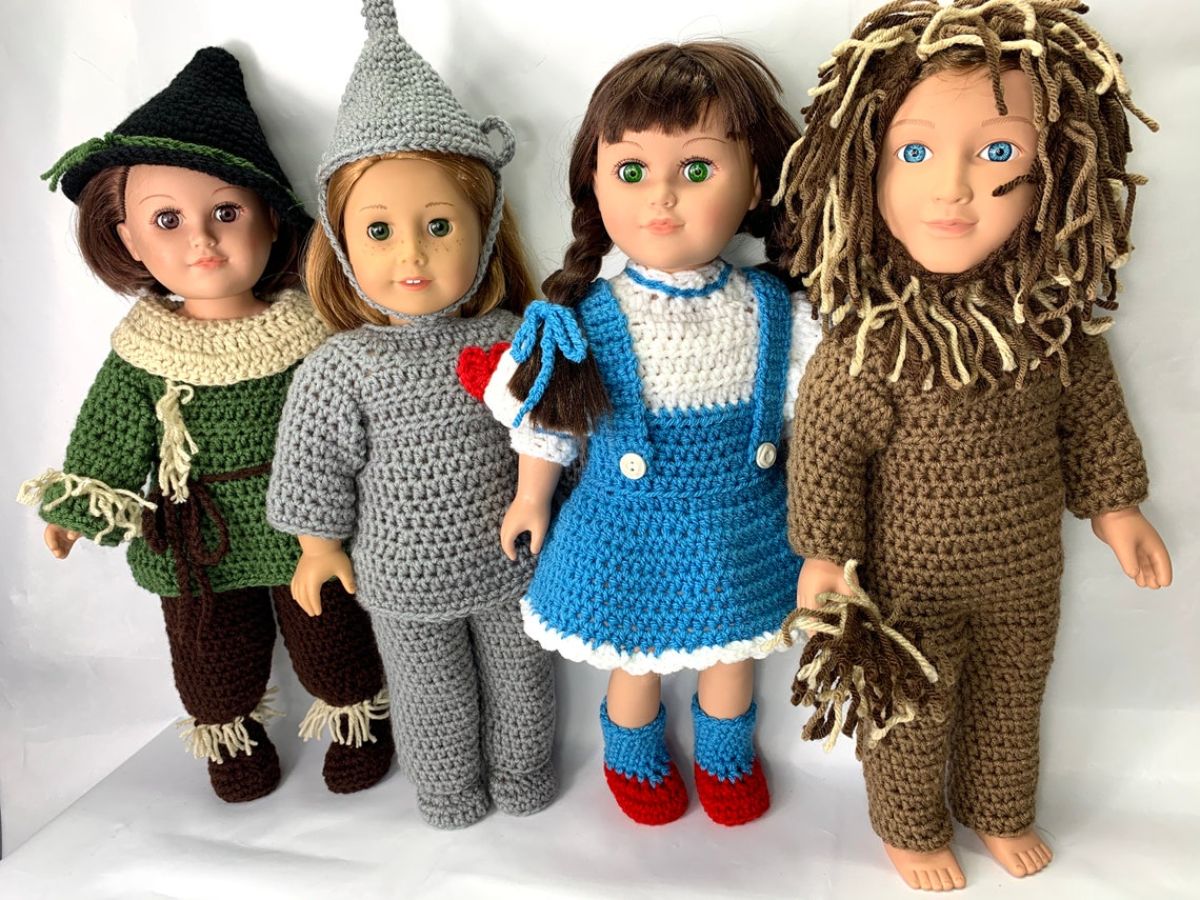 Four dolls wearing Wizard of Oz crochet costumes standing in a line as the scarecrow, tin man, Dorothy, and a lion.
