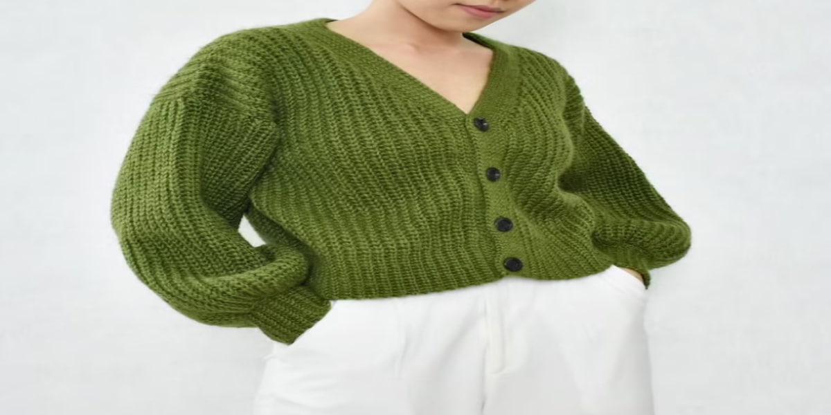 Woman wearing a cropped chunky green crochet cardigan with a v-neck and black buttons down the center.