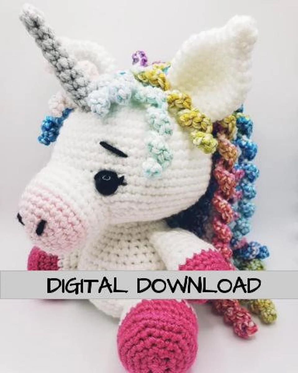 Large crochet stuffed unicorn with a light pink nose, bright pink feet, a green horn, and a curled multicolored mane.