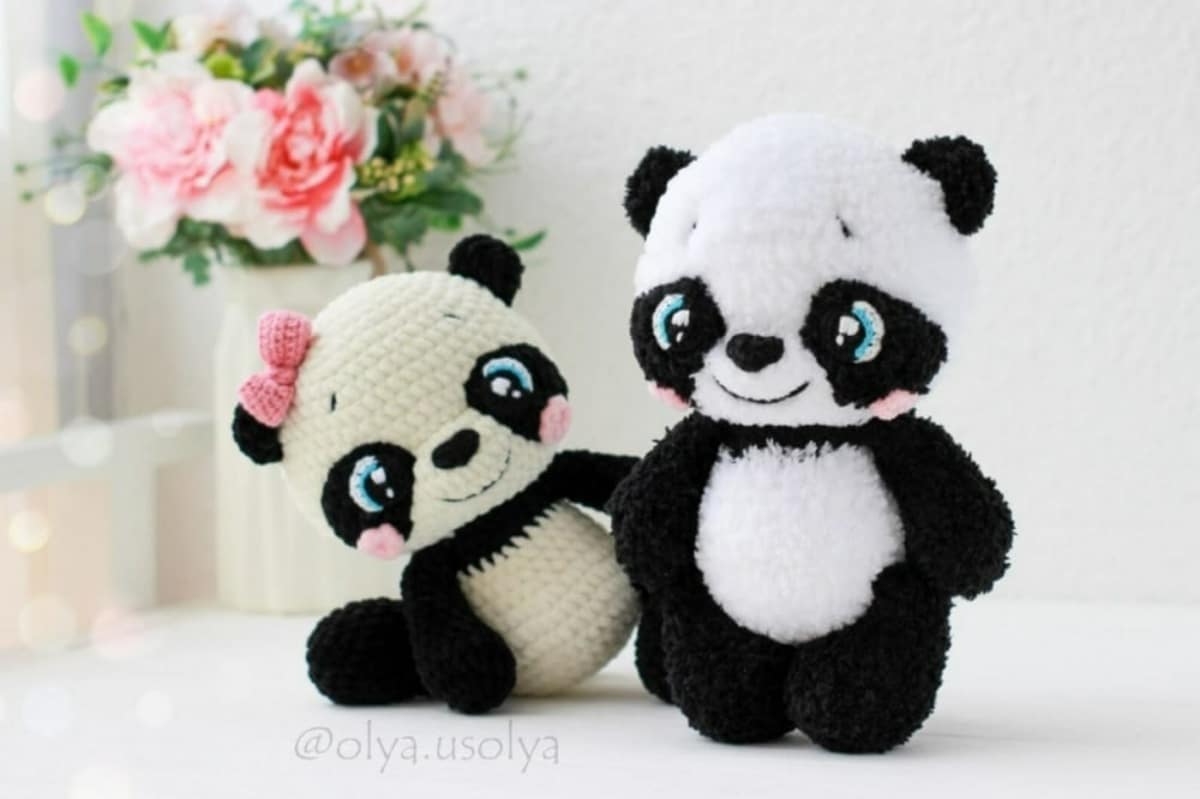 A boy black and white boy panda with blue cartoon eyes standing and a girl panda with the same features and a pink bow sitting next to him.