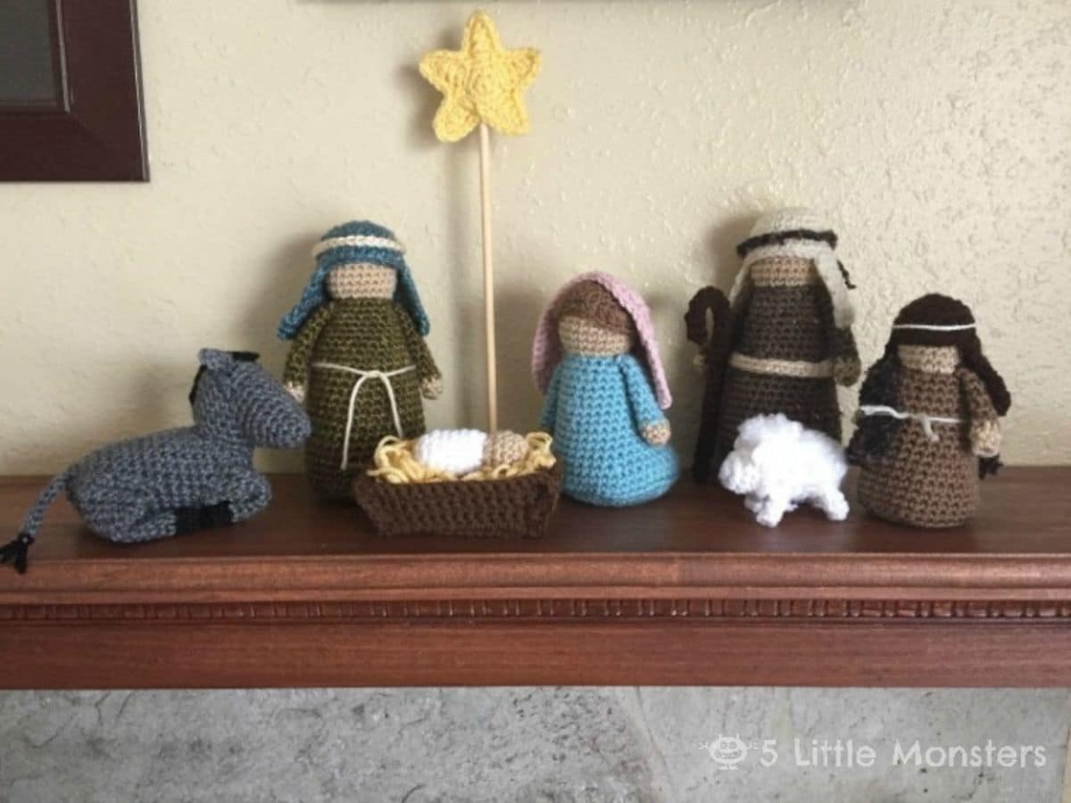 A small crochet nativity set of Mary and Joseph, a yellow star on a stand, two shepherds, some sheep, and Jesus in a manger.