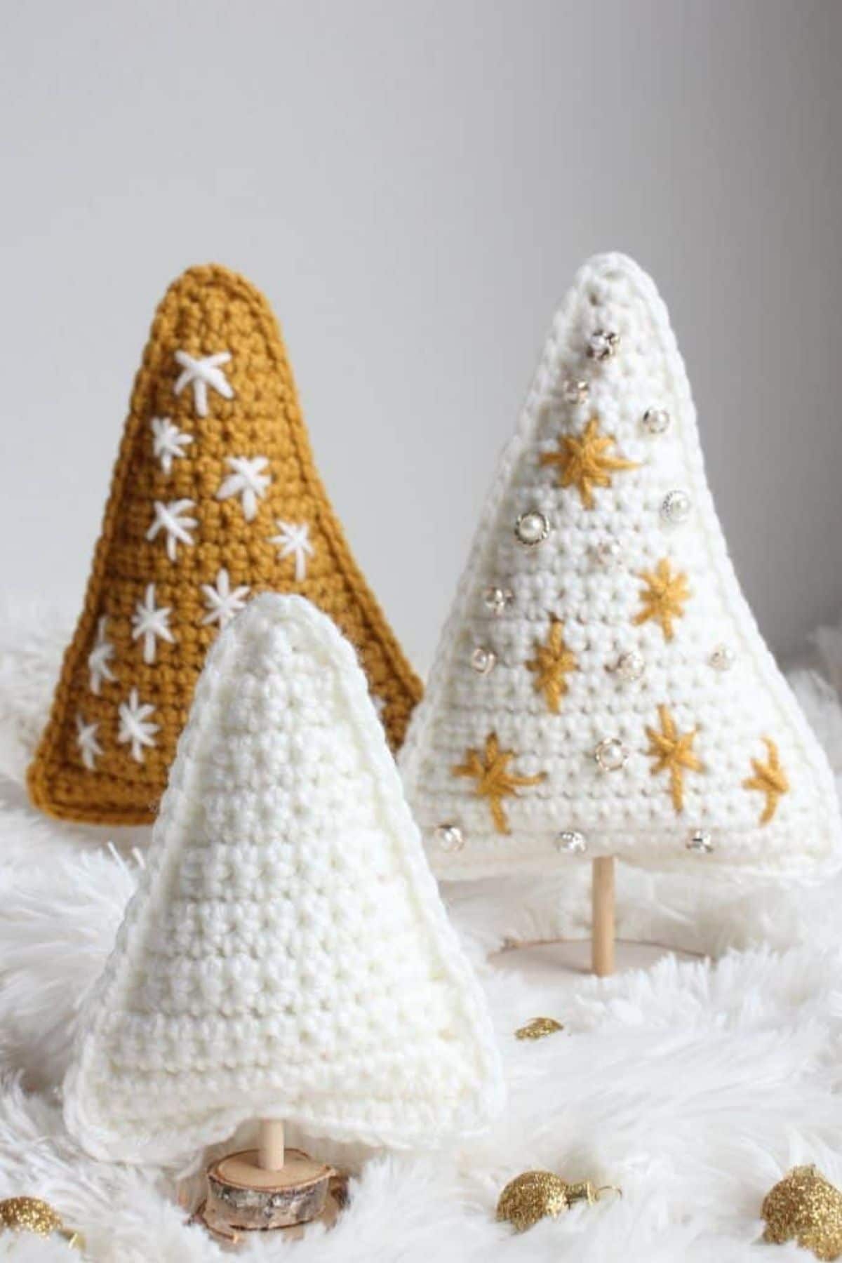 A white crochet Christmas tree on a wooden stand next to larger white and gold trees with stars stitched into them.