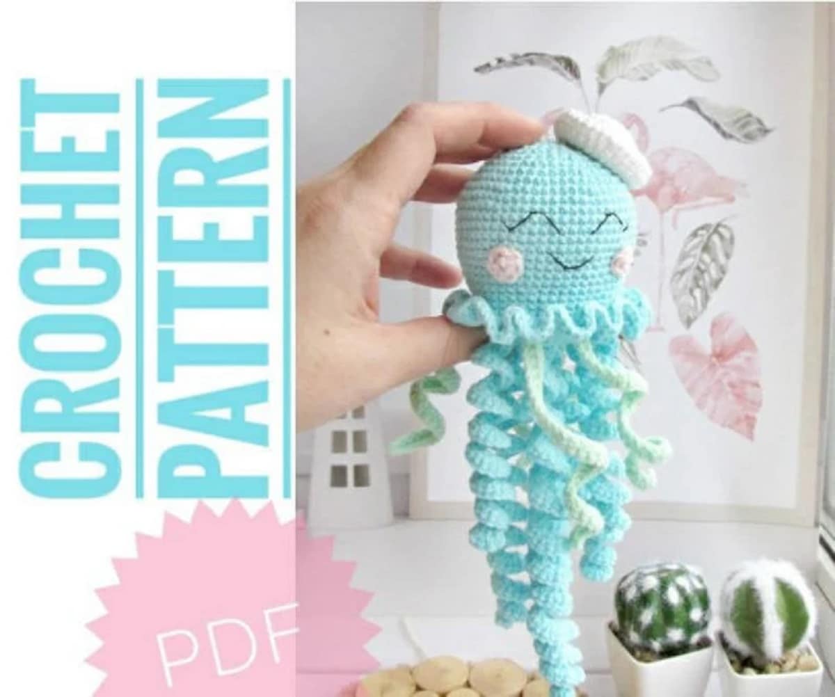 Small stuffed crochet baby style octopus with a light blue face, ruffle around its neck, and ruffle tentacles dangling from its head.