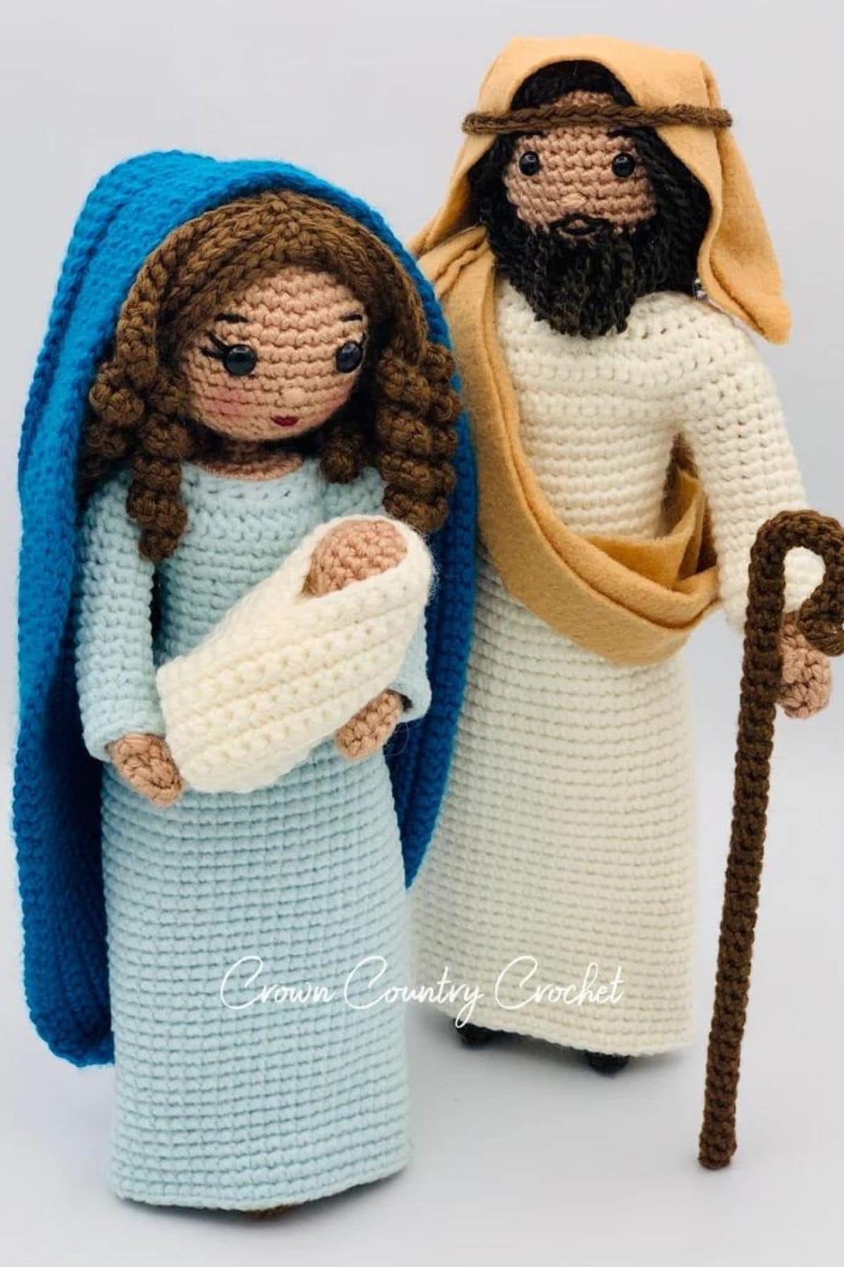 Large crochet Mary and Joseph dolls standing with Mary holding a baby Jesus in her arms in a white blanket.