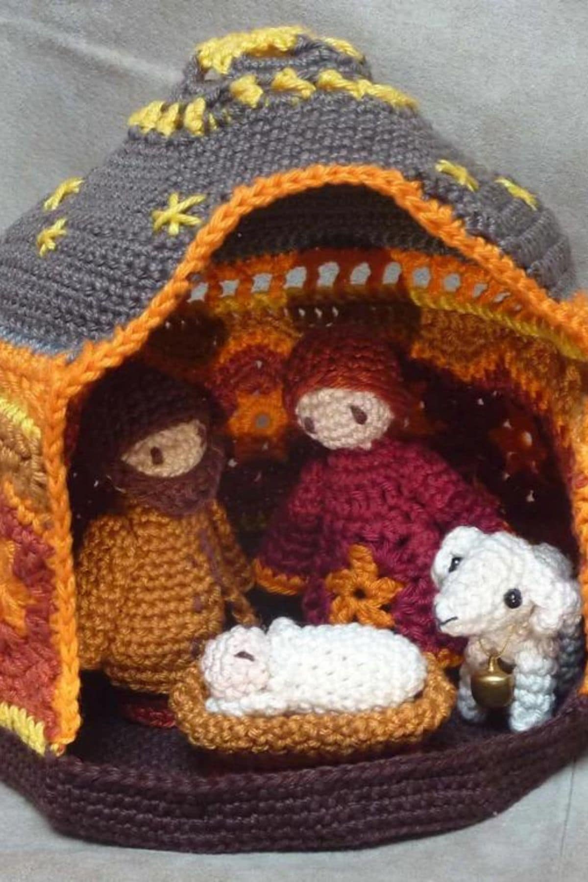 An orange and gray crochet structure covered in yellow stars with a small nativity scene using Mary, Joseph, and Jesus inside it.