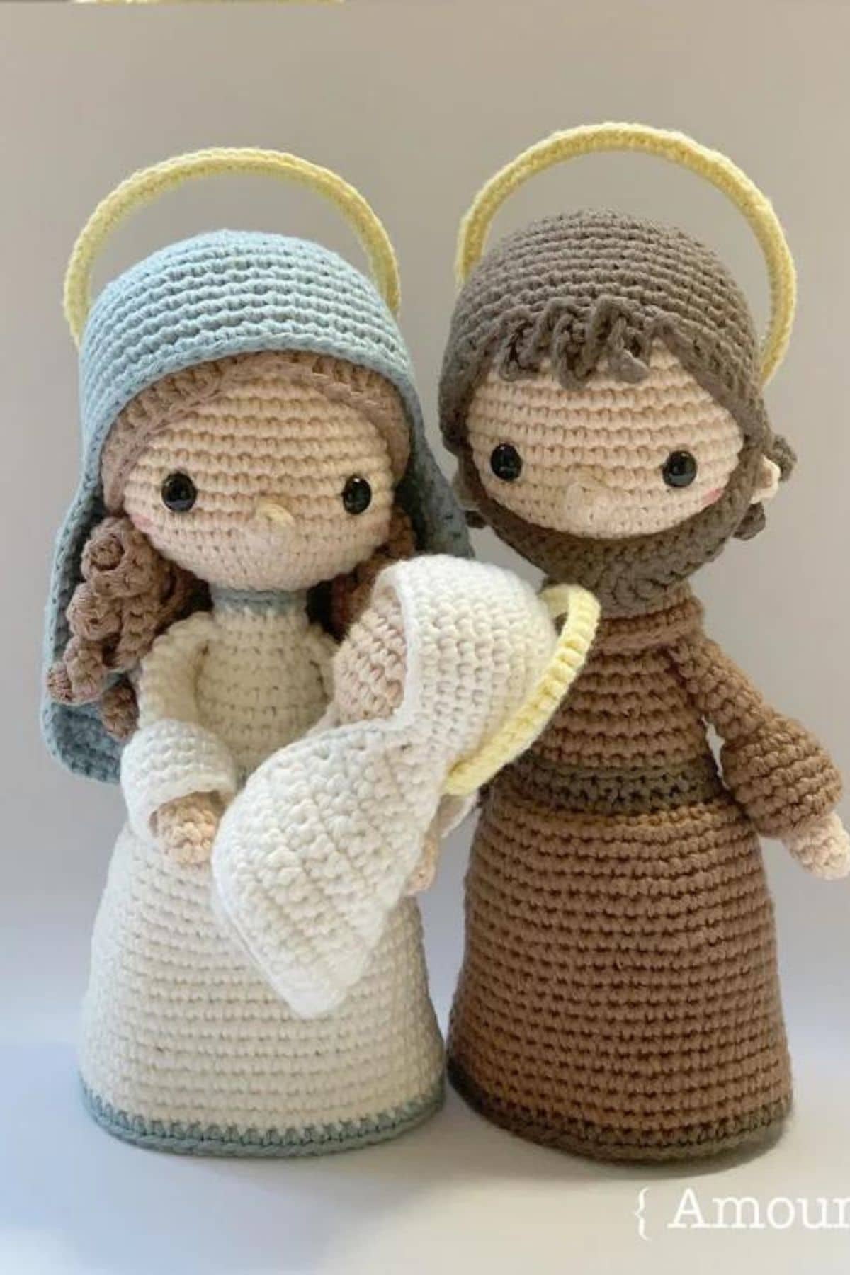 Large crochet Mary and Joseph in long white and brown dresses holding a small baby Jesus in a white blanket.