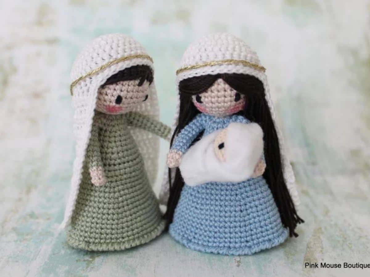 Small Mary and Joseph crochet dolls in blue and green dresses with Mary holding a white baby Jesus in her arms.