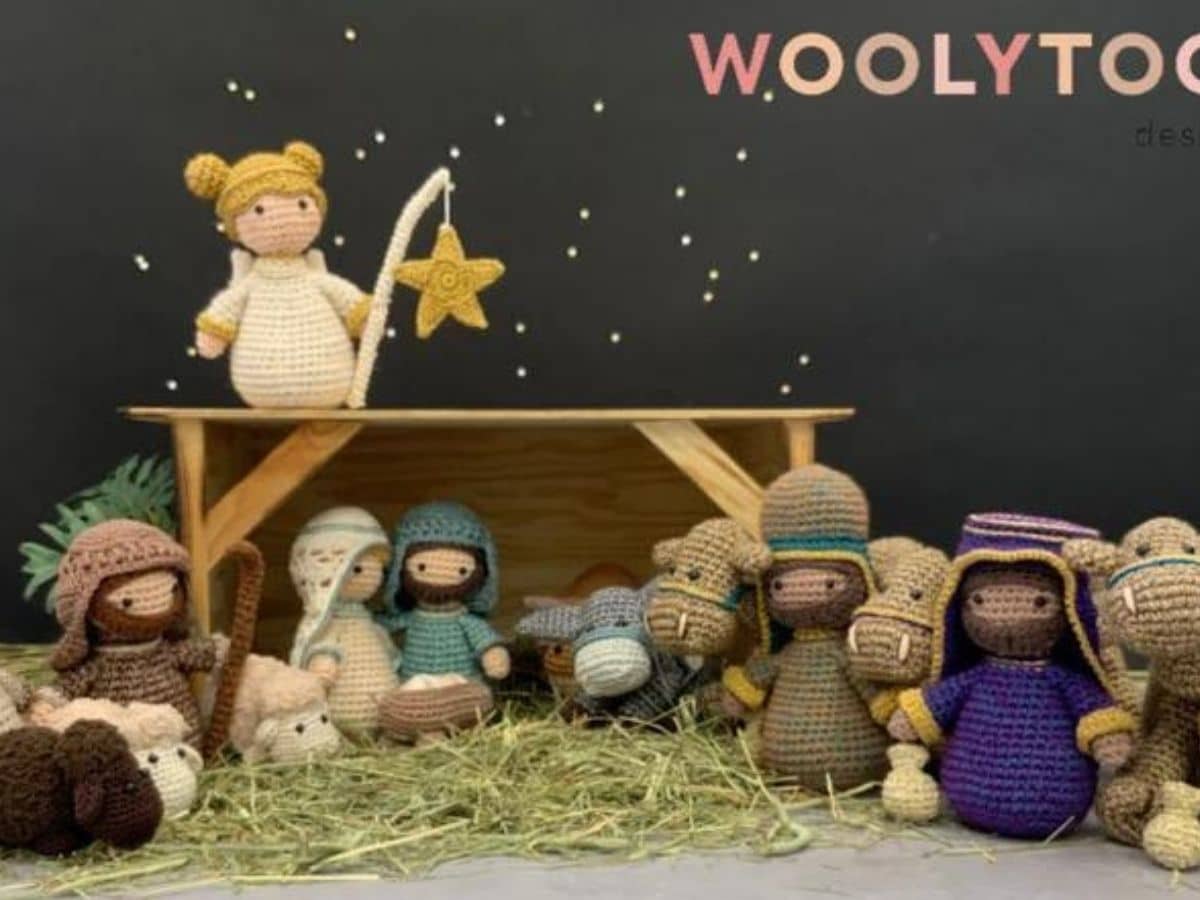 A wooden barn with a crochet nativity underneath and an angel standing on top with a yellow star hanging down.