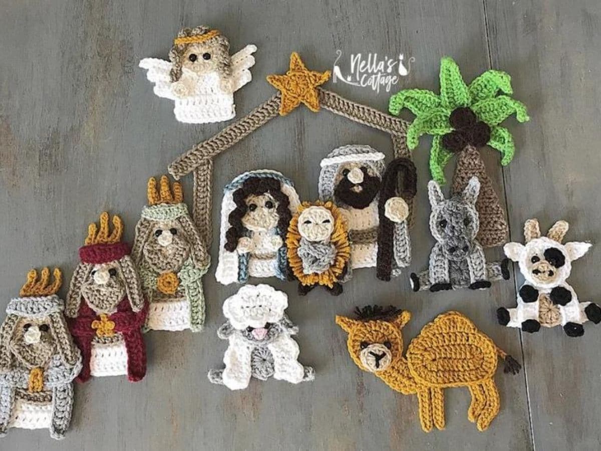 Crochet nativity scene lying flat with a wooden barn in the background and cows, camels, donkeys, and sheep surrounding the dolls.