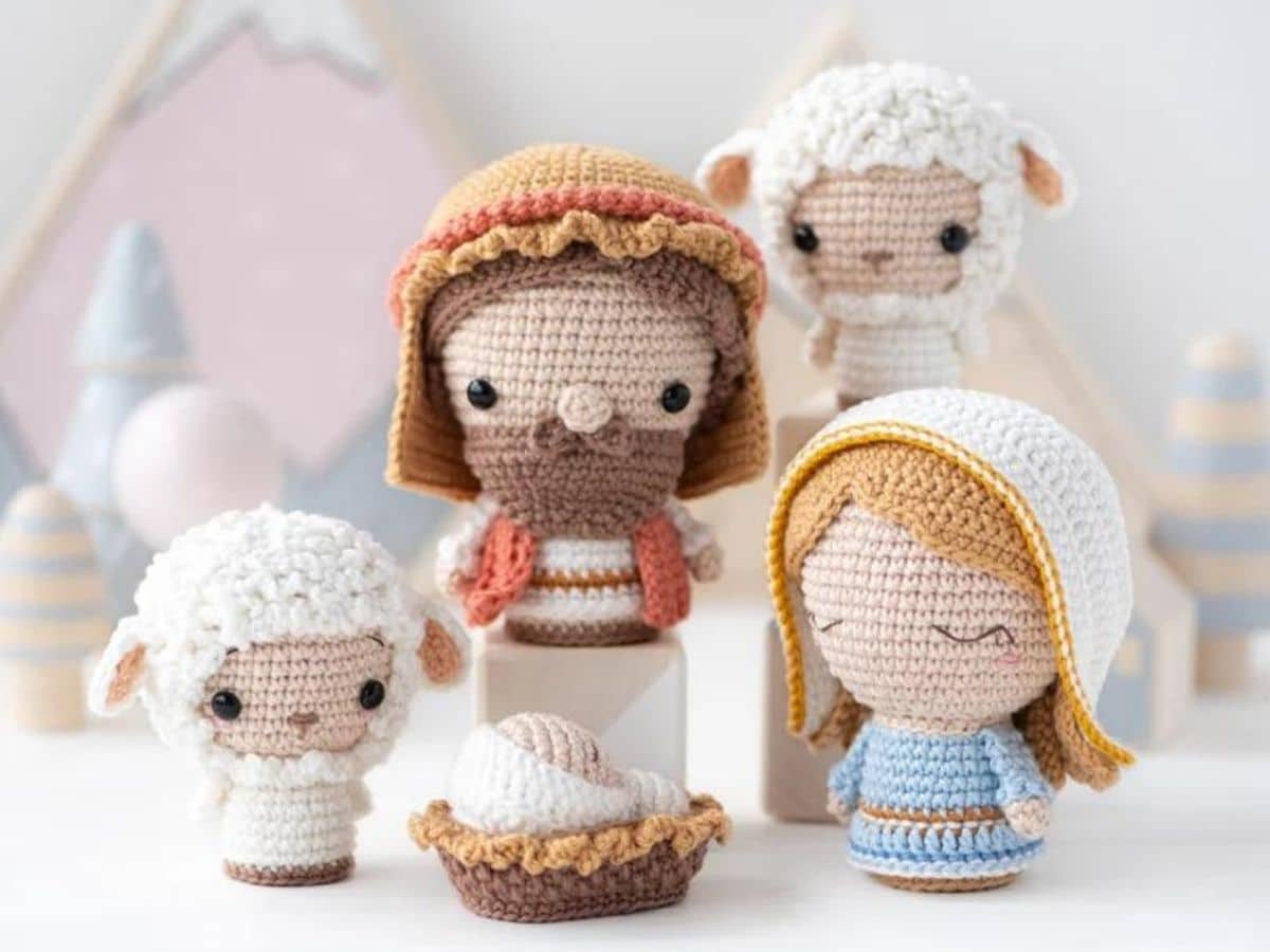 Small crochet Mary doll standing next to a tall Joseph and two small sheep with a baby Jesus in a manger at their feet.