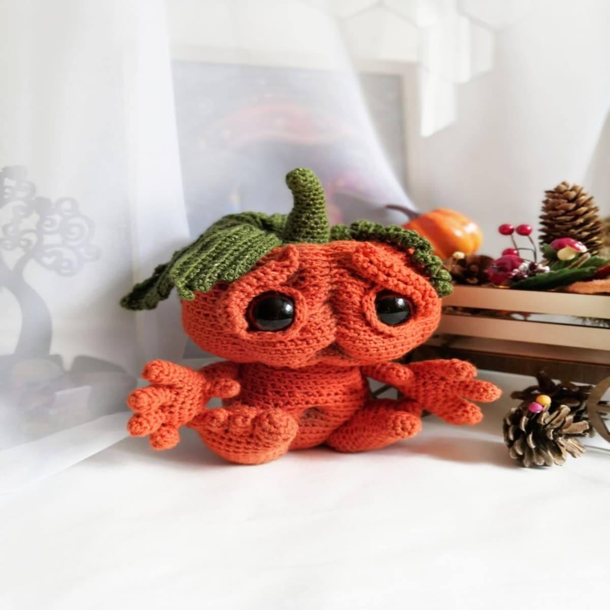 Orange crochet pumpkin monster with large orange hands and feet and a green stem and large leaves on its head.