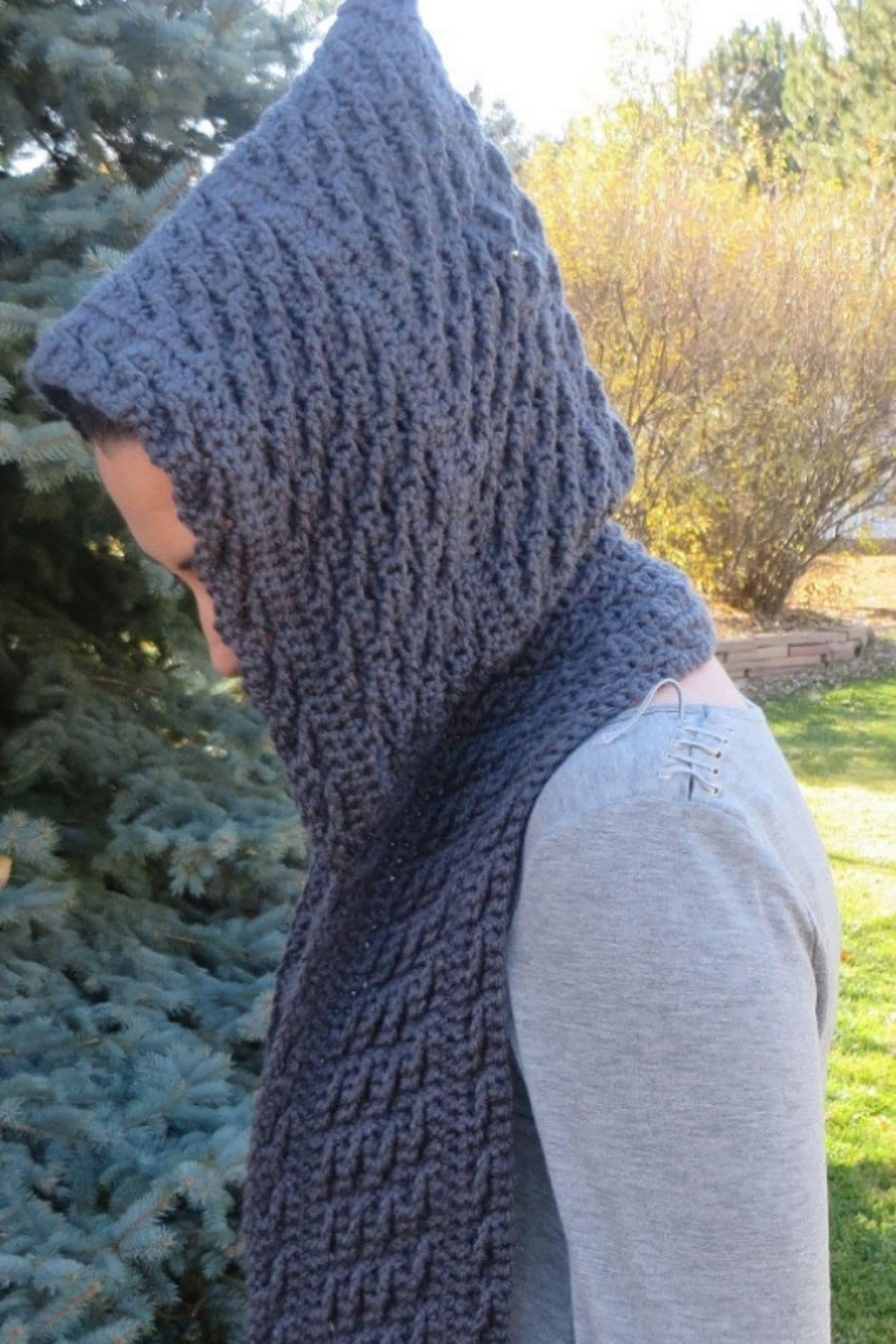 Young woman outside standing sideways wearing a gray crochet hooded scarf.