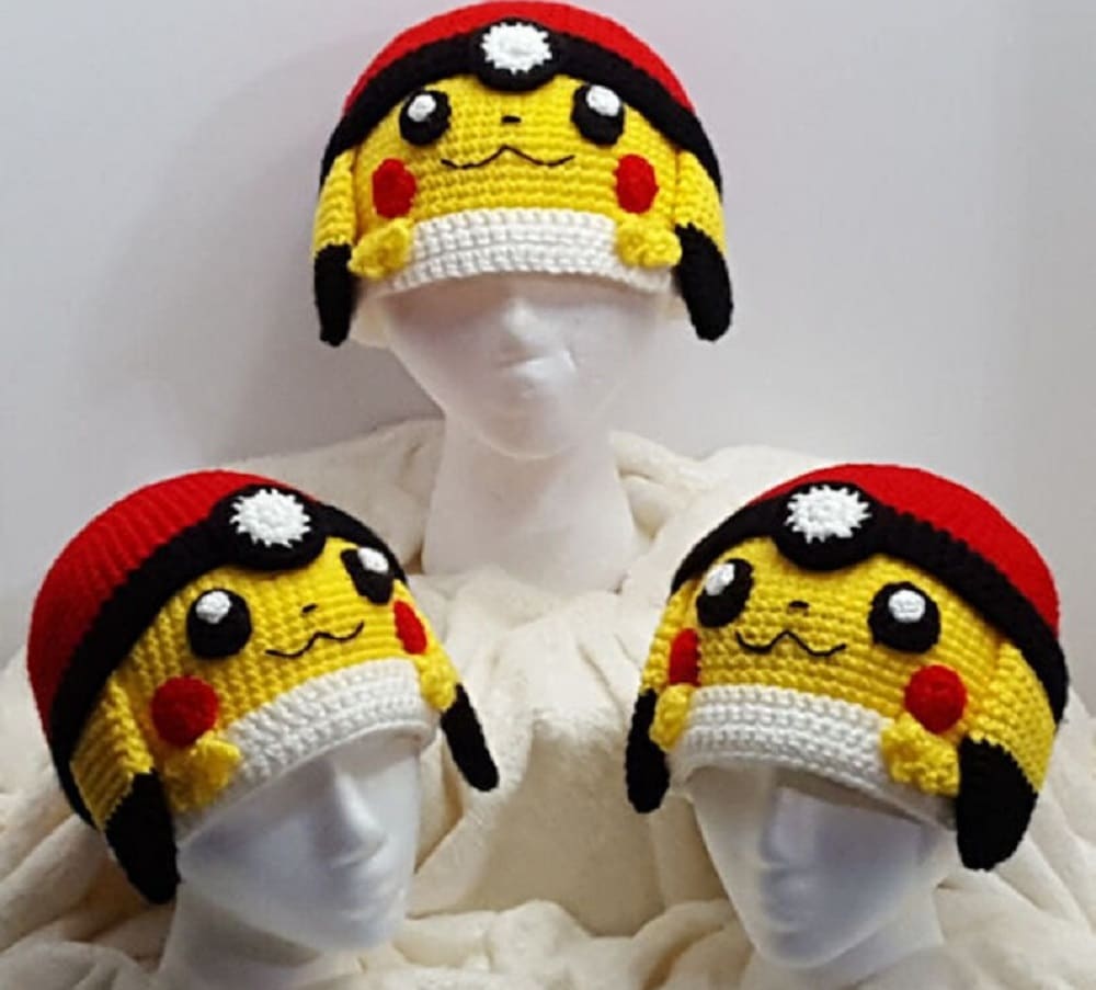 Three mannequins wearing a crochet Pickachu beanie hat with a Pokeball stretched across the top, Pickachu’s face, and ears dangling down the side. 