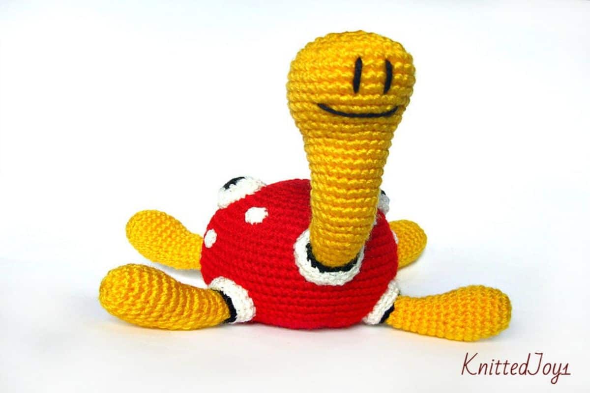 Crochet Shuckle with a white head and legs and a red and white body sitting with its legs spread on a white background.