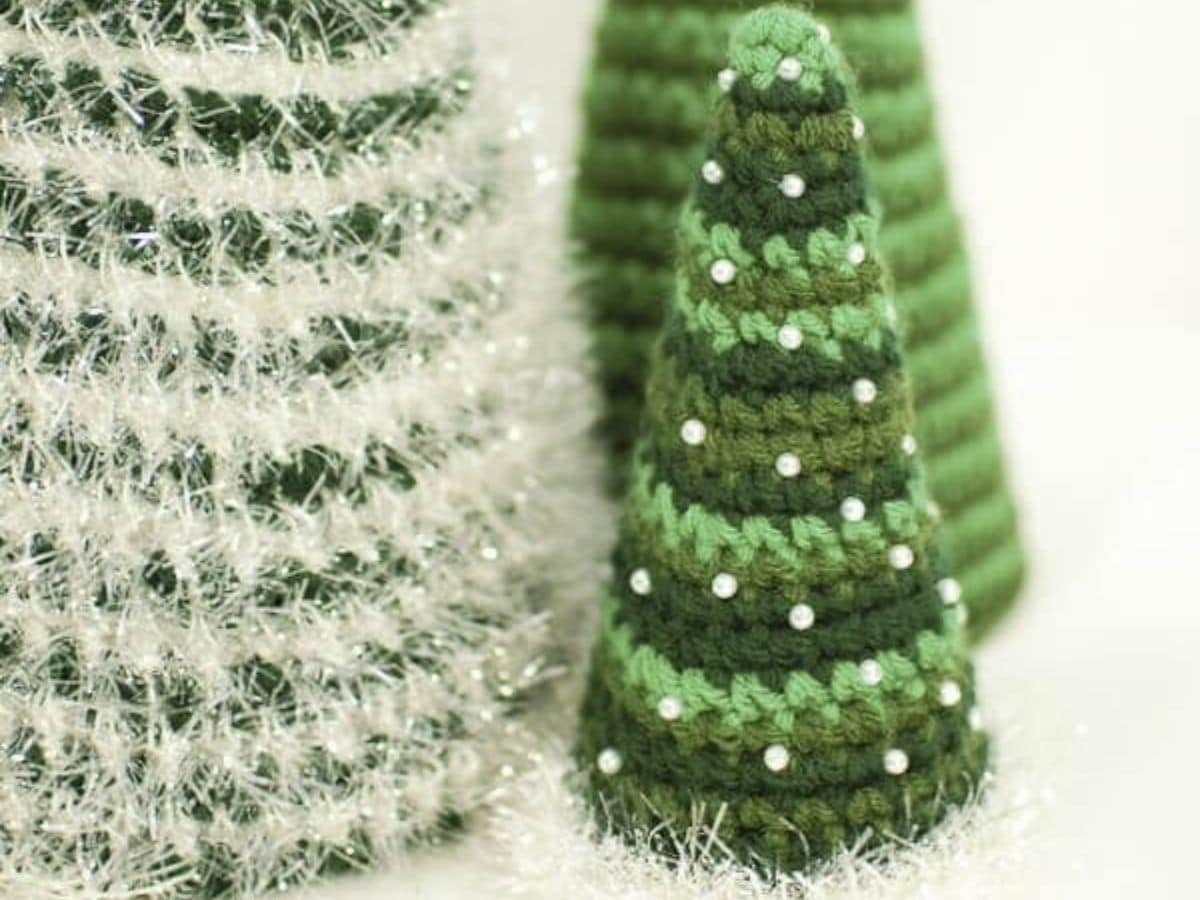 A green, dark green, and light green striped crochet Christmas tree next to a larger white and green fluffy tree.