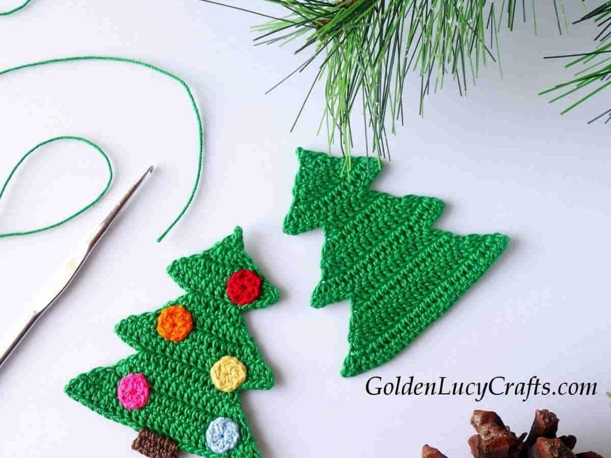 A green crochet Christmas tree with pink, orange, and yellow circles on, next to a plain tree on a white table.