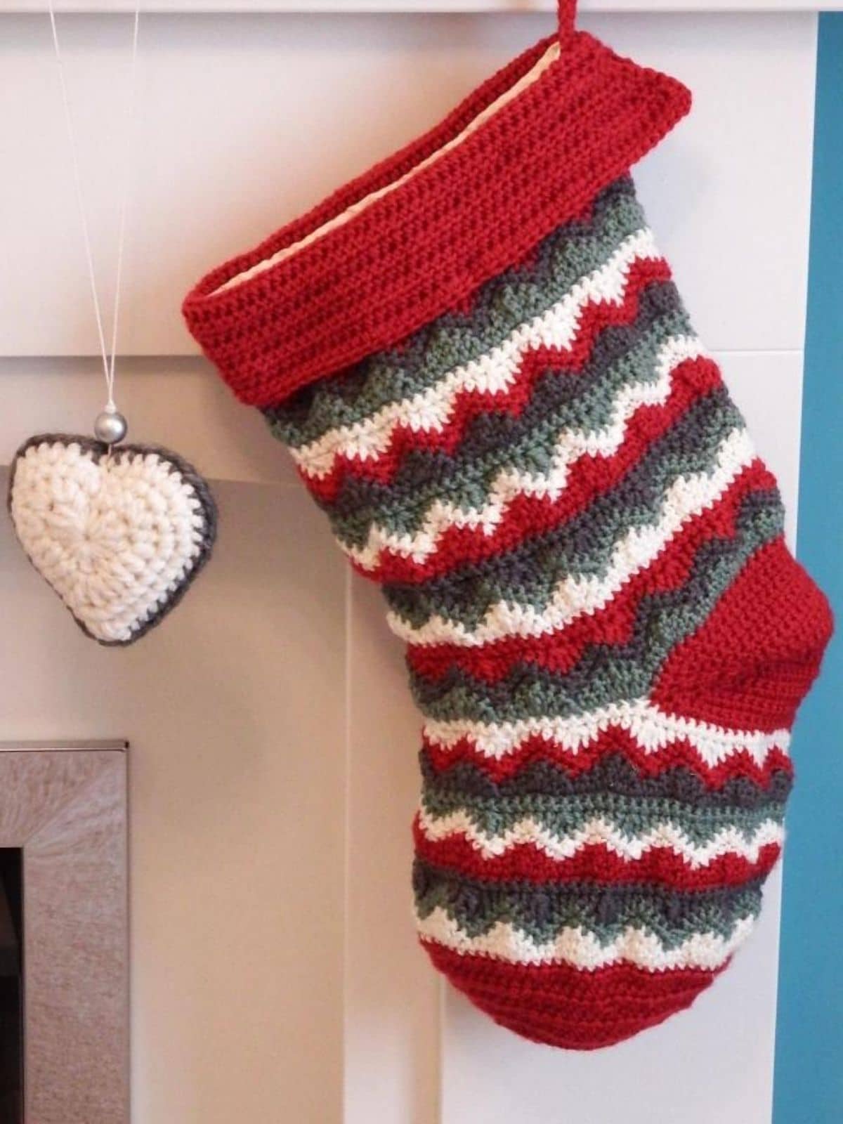 Zig-zag red white and green stocking hanging from a mantle next to a white heart decoration.