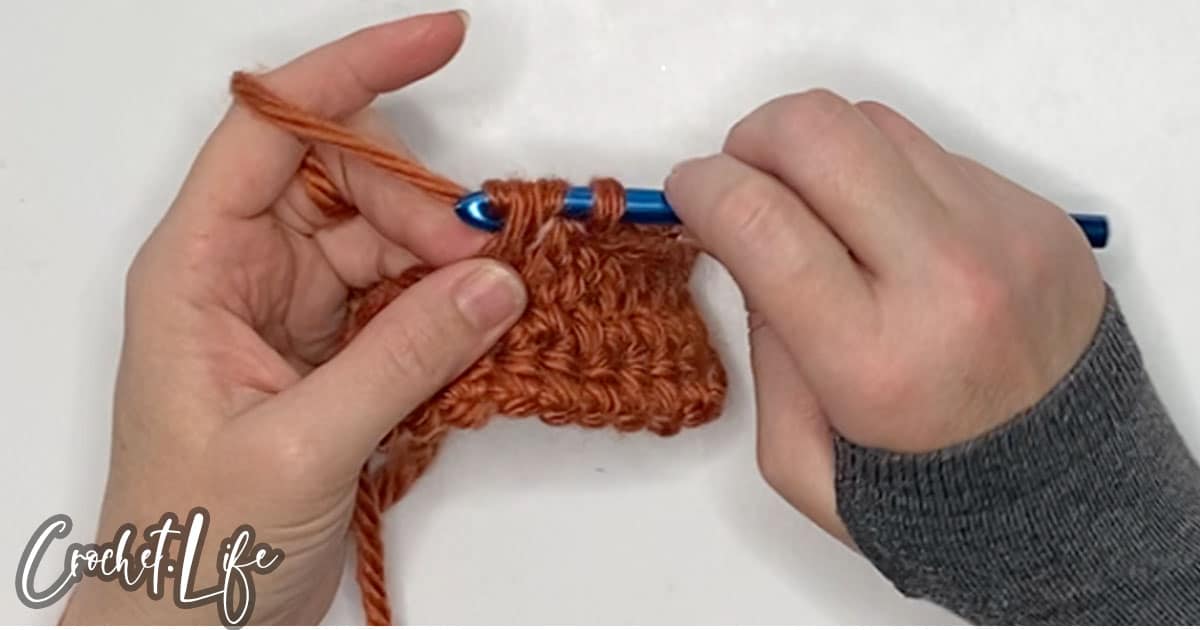 in-process step of making a half double crochet stitch to make a fall pumpkin crochet pattern